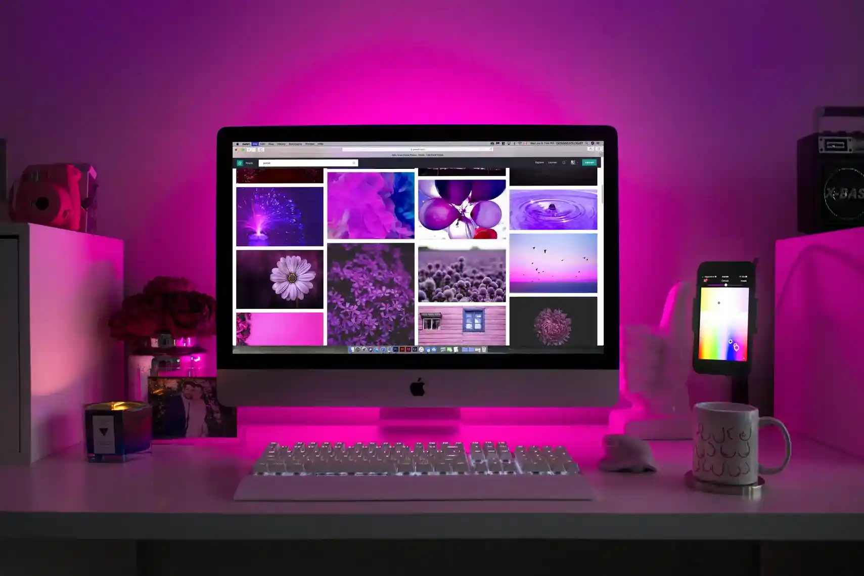 Desktop setup with iMac displaying purple images, illuminated by pink LED backlighting and surrounded by desk accessories